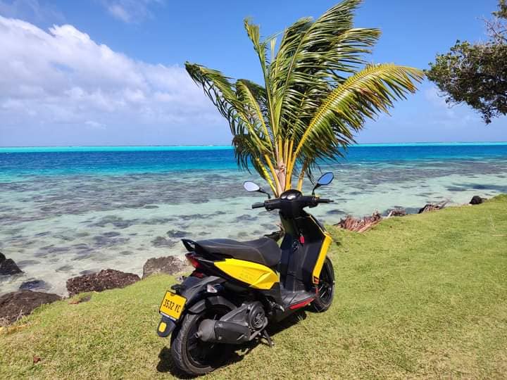 Scooter jaune devant le lagon turquoise de Huahine